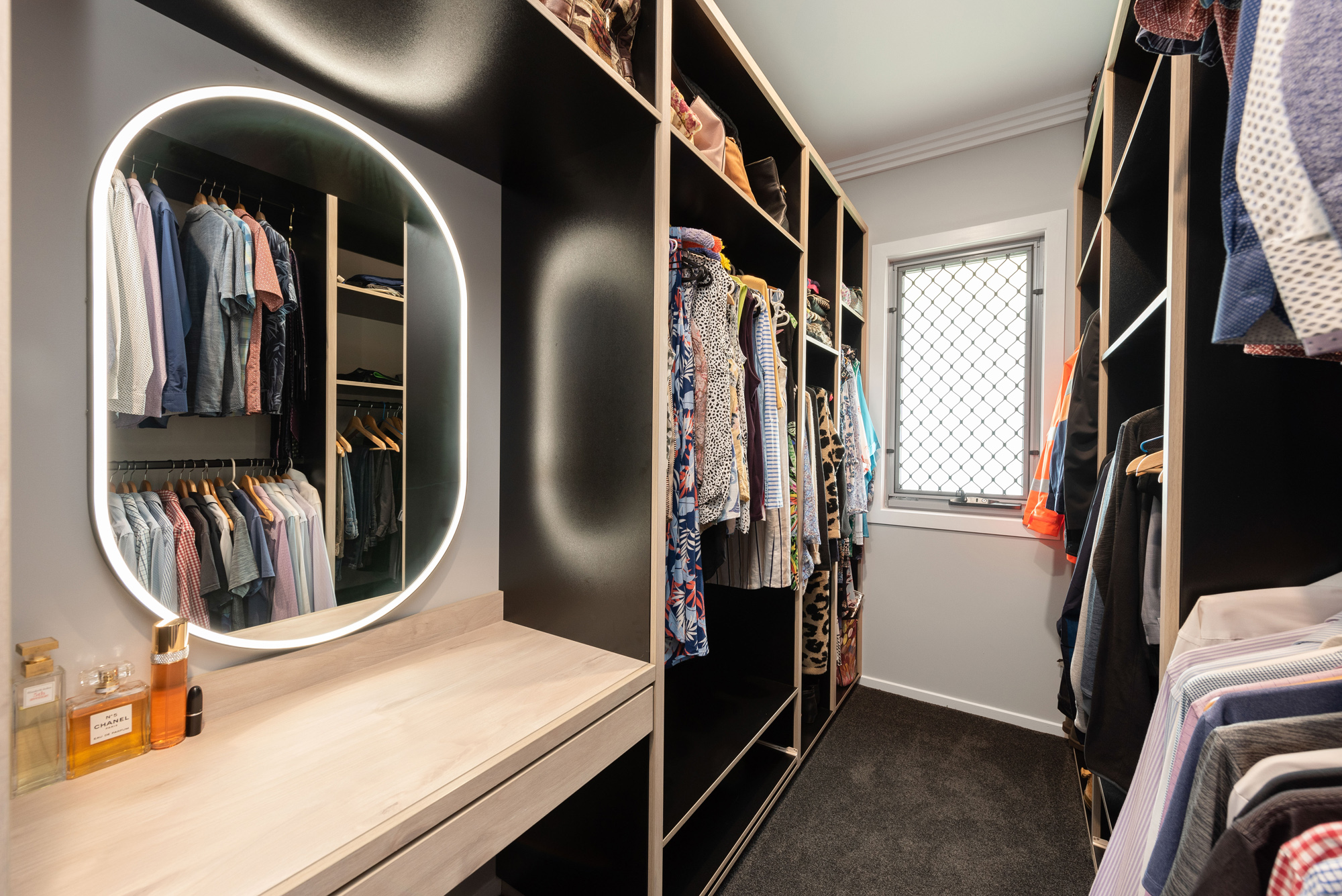 Custom woodgrain and black walk in wardrobe with oval mirror and integrated lighting